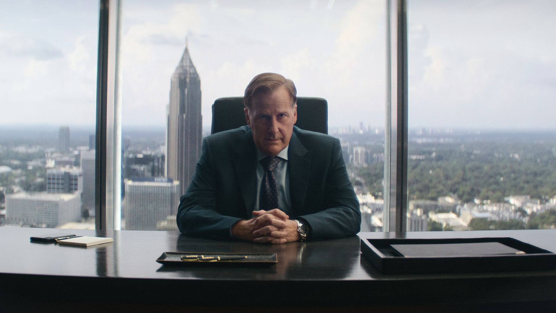 Jeff Daniels looks concerned and sits at a desk in a high rise tower