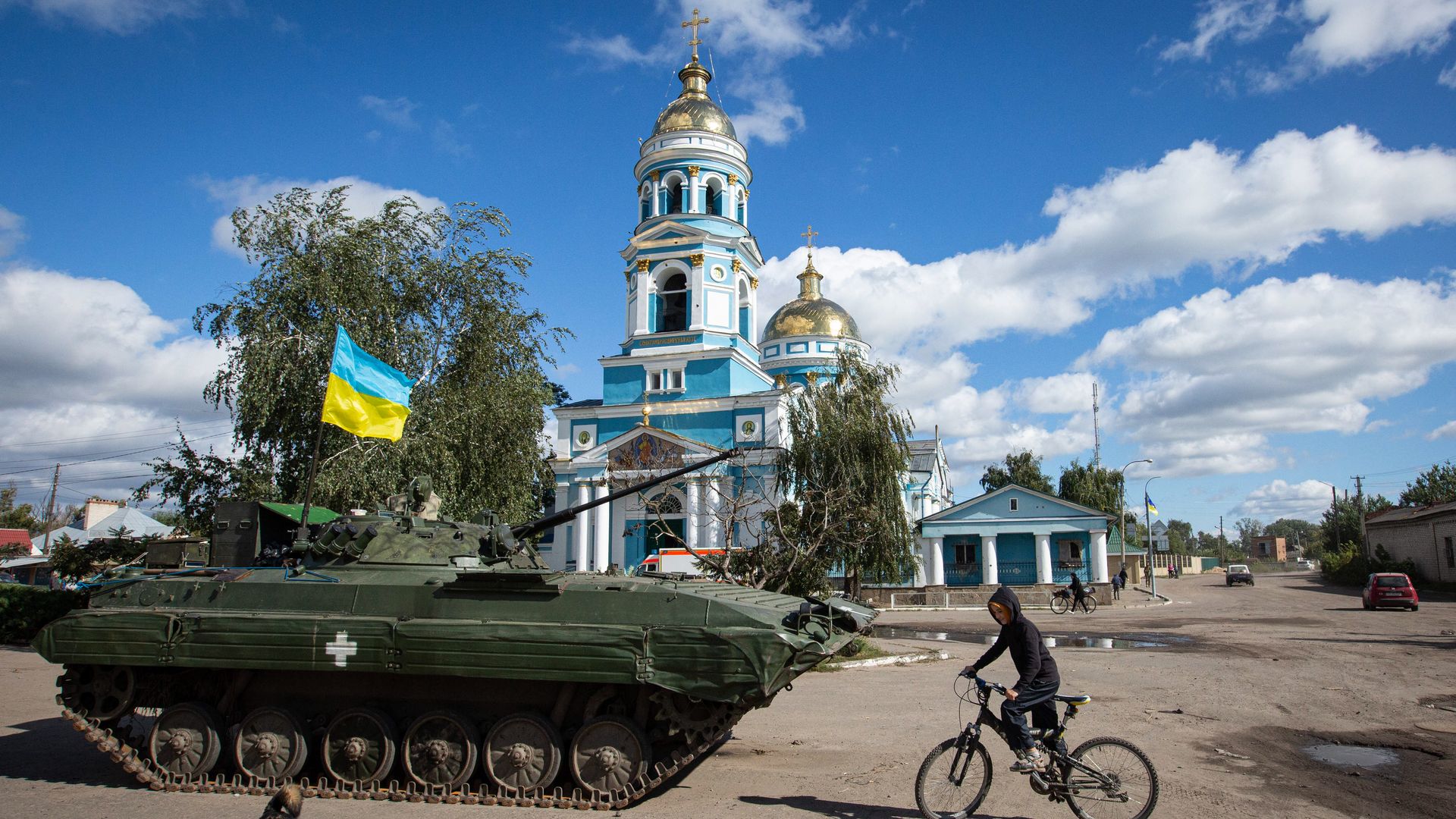 A boy rides a bicycle near an armored tank with a Ukrainian flag in the town of Izium, recently liberated by Ukrainian Armed Forces, in the Kharkiv region
