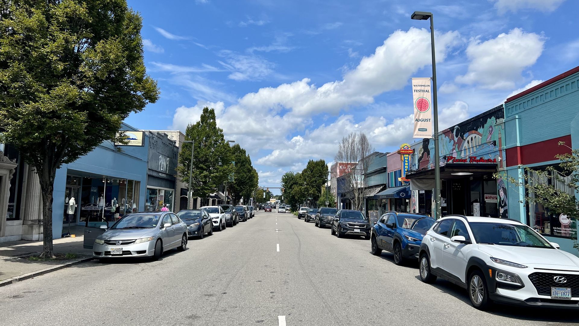 A tree-lined street with parked cars on either side next to businesses.