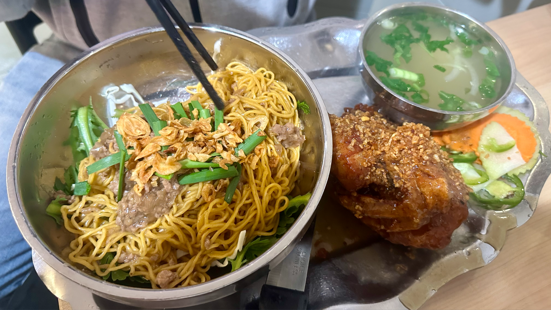 A bowl of dry egg noodles next to garlic fried chicken and broth and salad from The Boat.