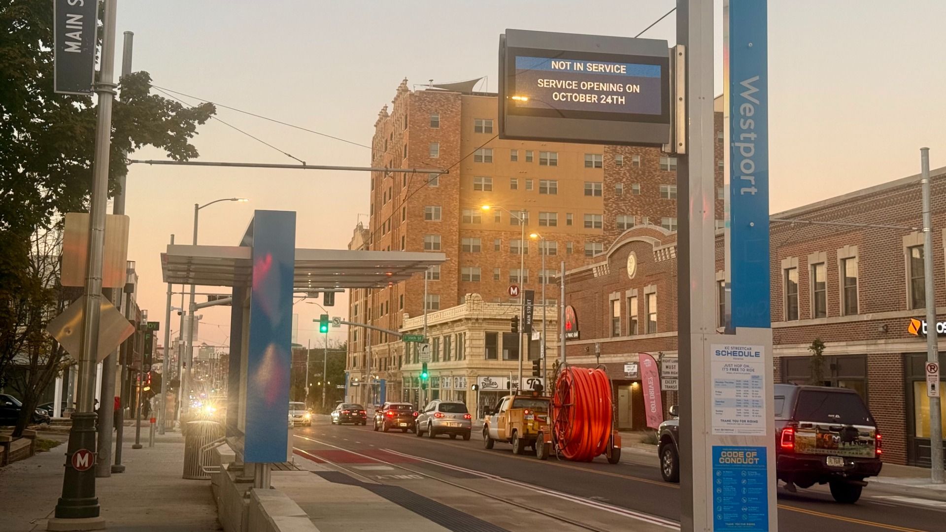 Street view at dusk showing the Westport transit stop with a "Not in Service" sign, cars on the road, and buildings with classic brick and stone facades in the background.