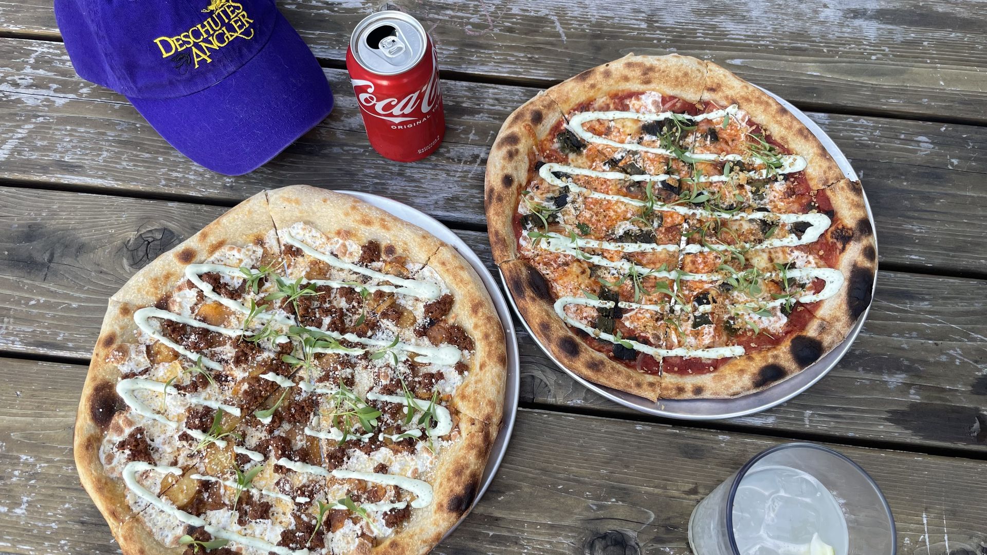 A photo of two pizzas on a wood grain table.