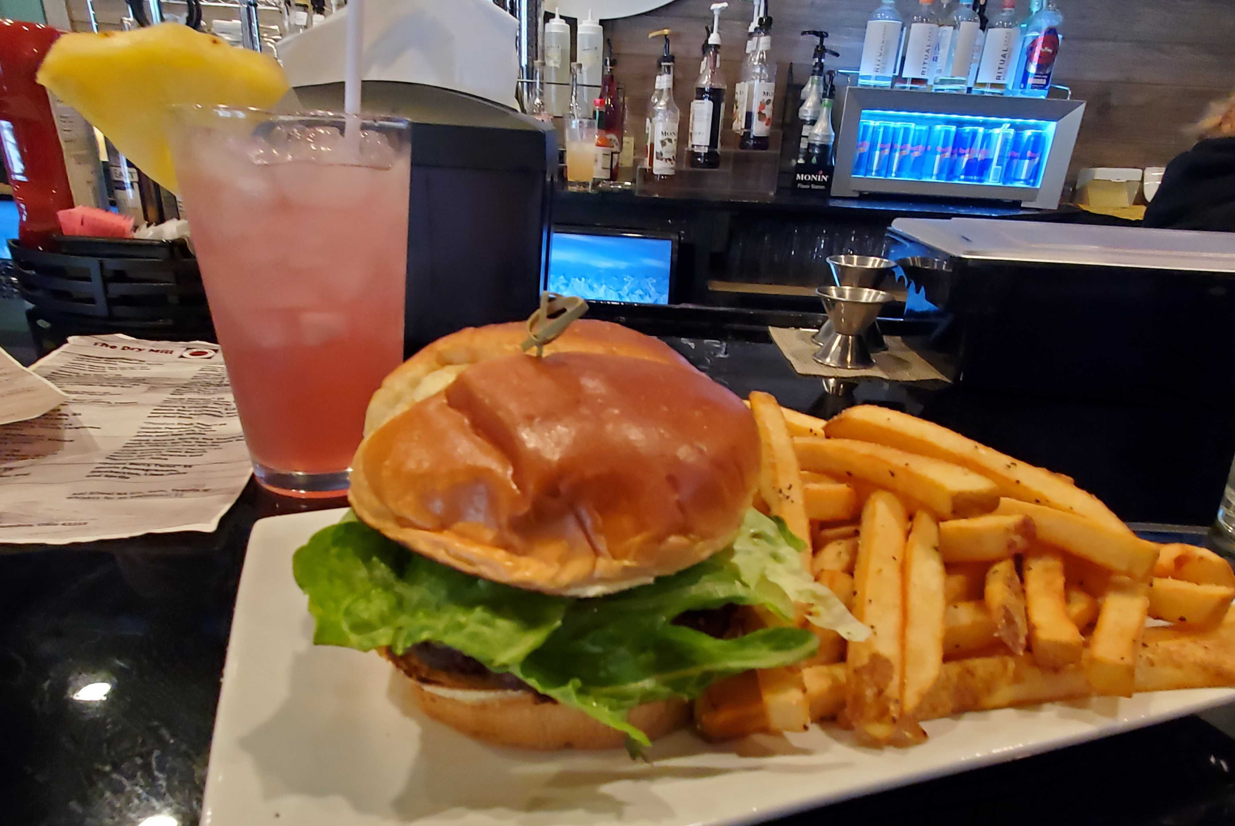 A sweet potato quinoa burger, fries and a non-alcoholic cocktail at a bartop. 