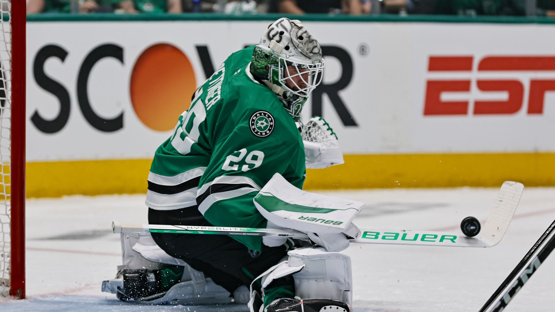 A player in green protective gear balances a puck on his hockey stuck