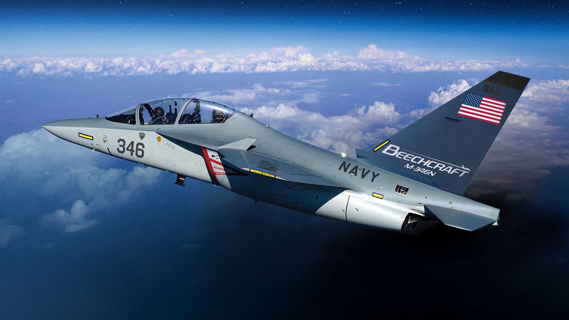 Gray two-seat military jet flying above clouds with canopy open; markings read 346 and NAVY, US flag on the tail, Beechcraft branding on the fuselage against a deep blue sky.