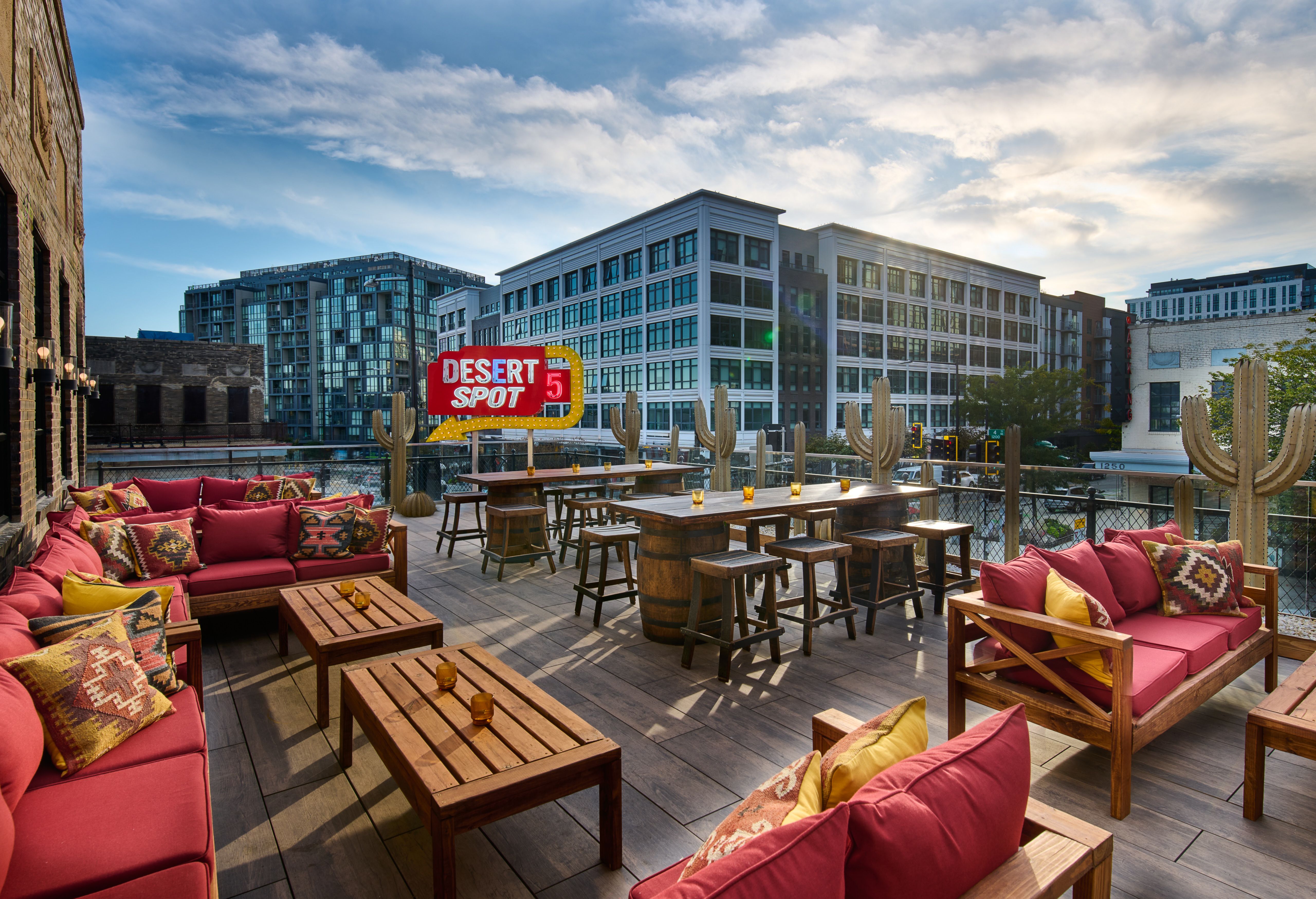 An outdoor rooftop bar with pink counches, yellow desert-style pillows and cacti 