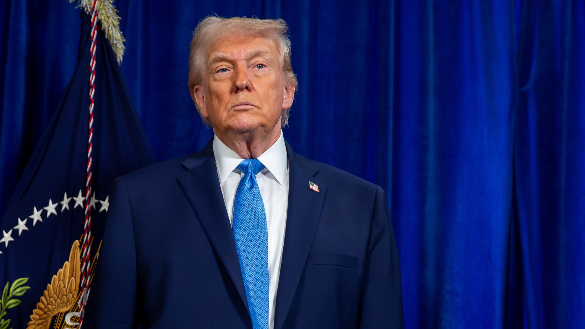 President Trump stands in front of a blue curtain.