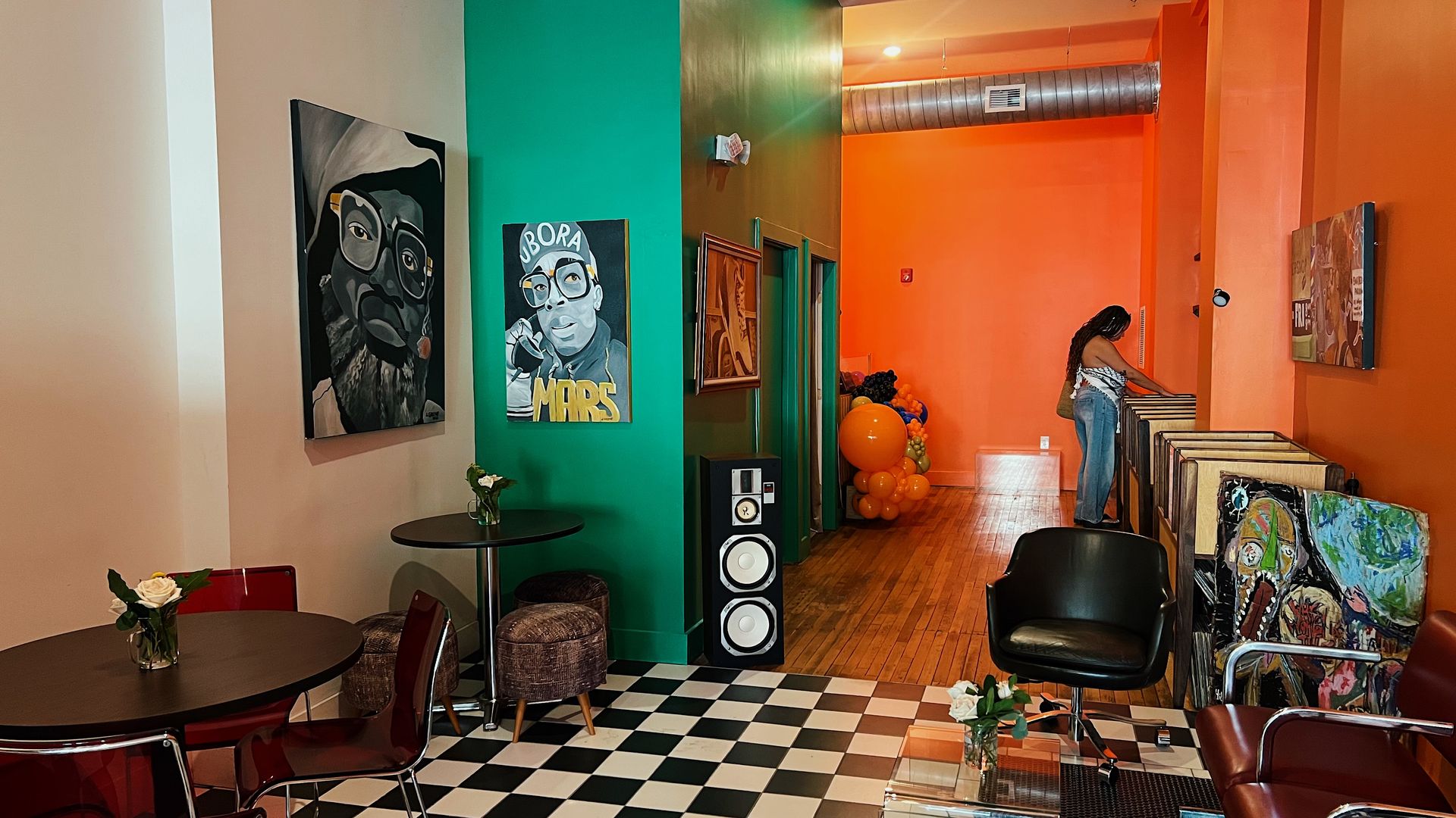 a coffee shop with black and white tiles, an orange wall on the right covered in artwork and vinyl records