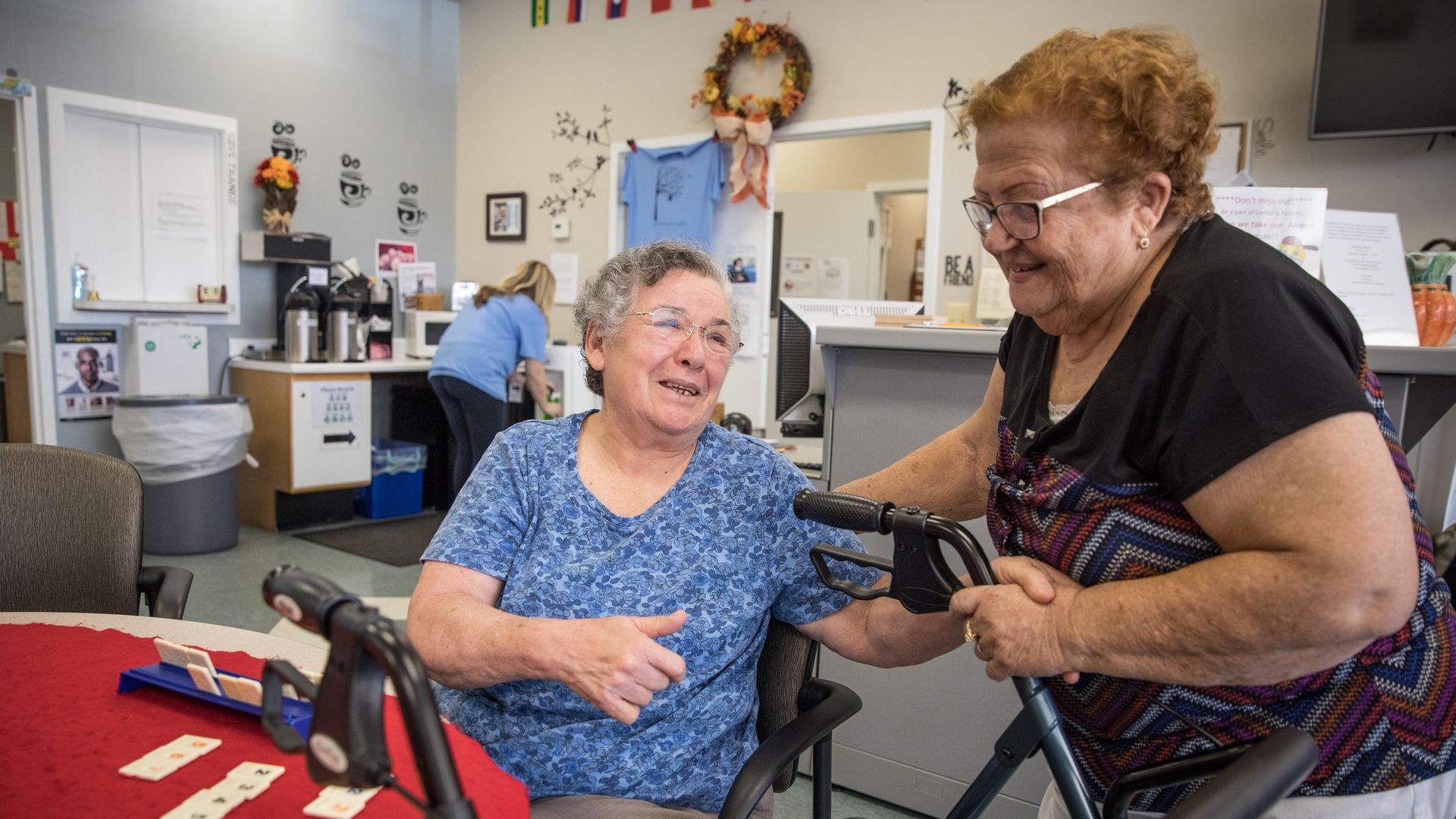 Two older women sit near a table at a senior center.