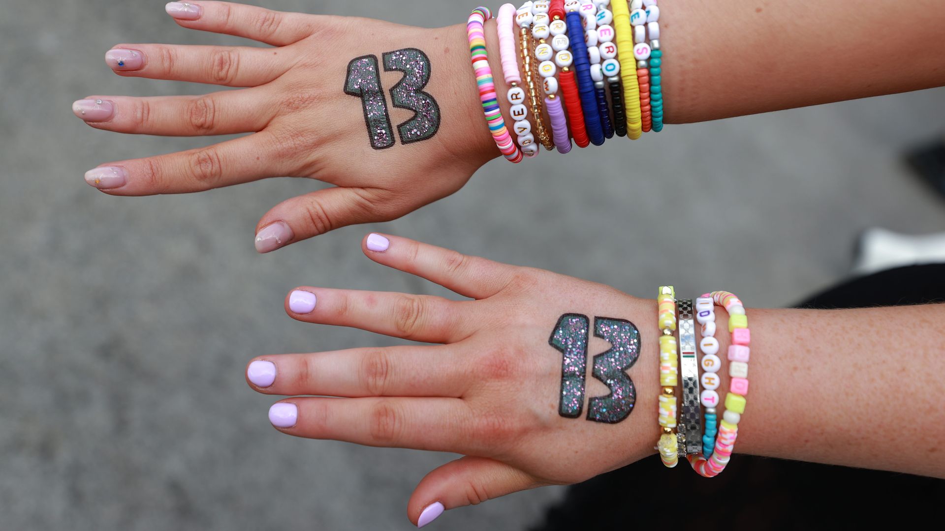 A photo of the top of two outstretched hands. Both have the number 13 written in glittery marker and wear friendship bracelets.