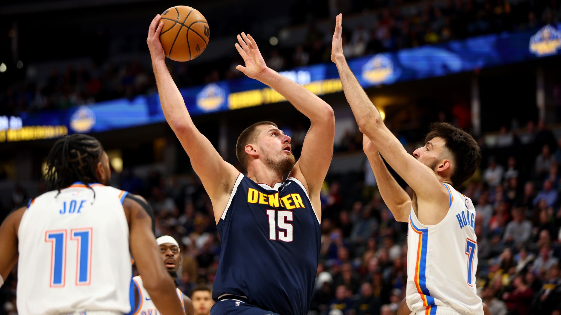 A man drives up with a basketball attempting to score while another reaches his hands up trying to stop him. 
