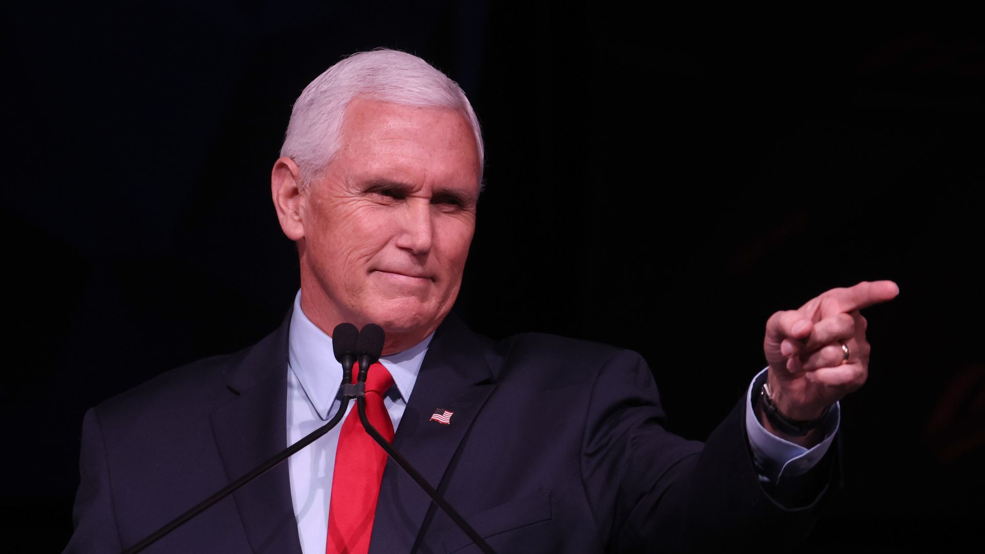 Former Vice President Mike Pence smiles from a podium and points at someone with his left hand index finger