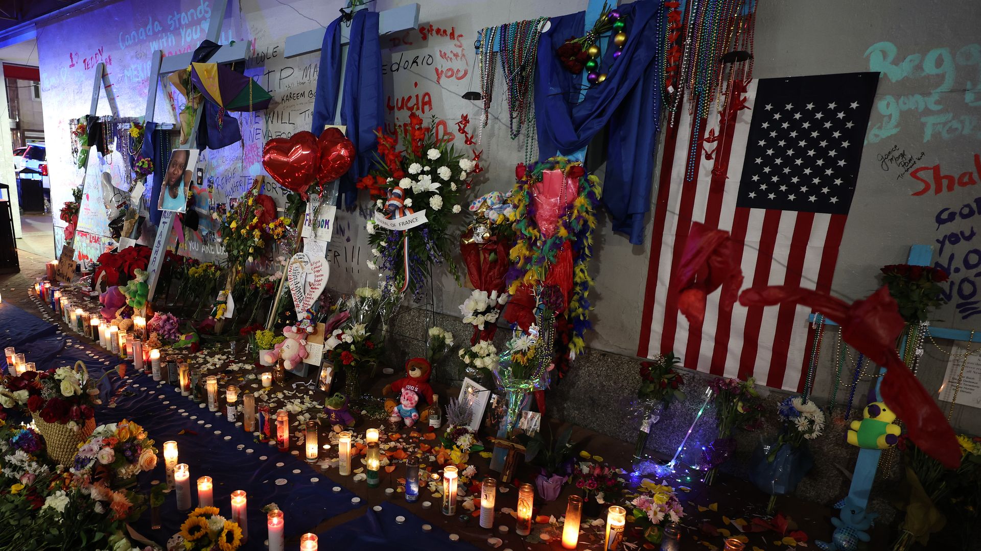 A photo of a makeshift memorial with two rows of lit candles, crosses, flowers, an American flag and other mementos.
