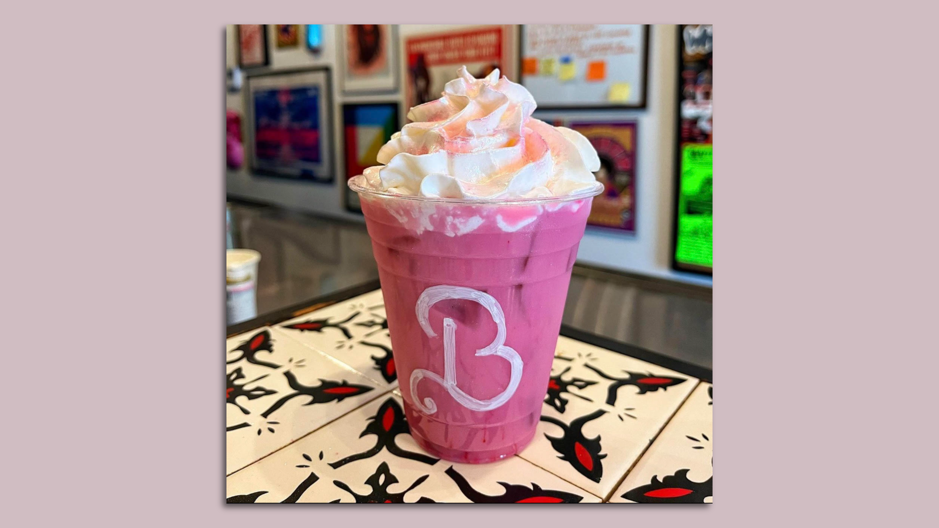 A bright pink coffee drink with a fancy letter B painted on the cup, and topped with whipped cream.