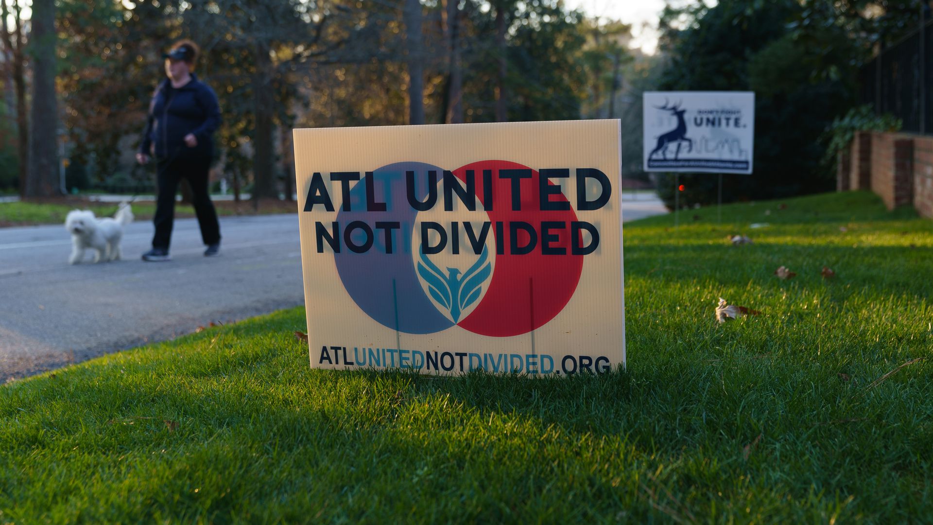 A woman walks a dog next to a sign that says "ATL United Not Divided" 