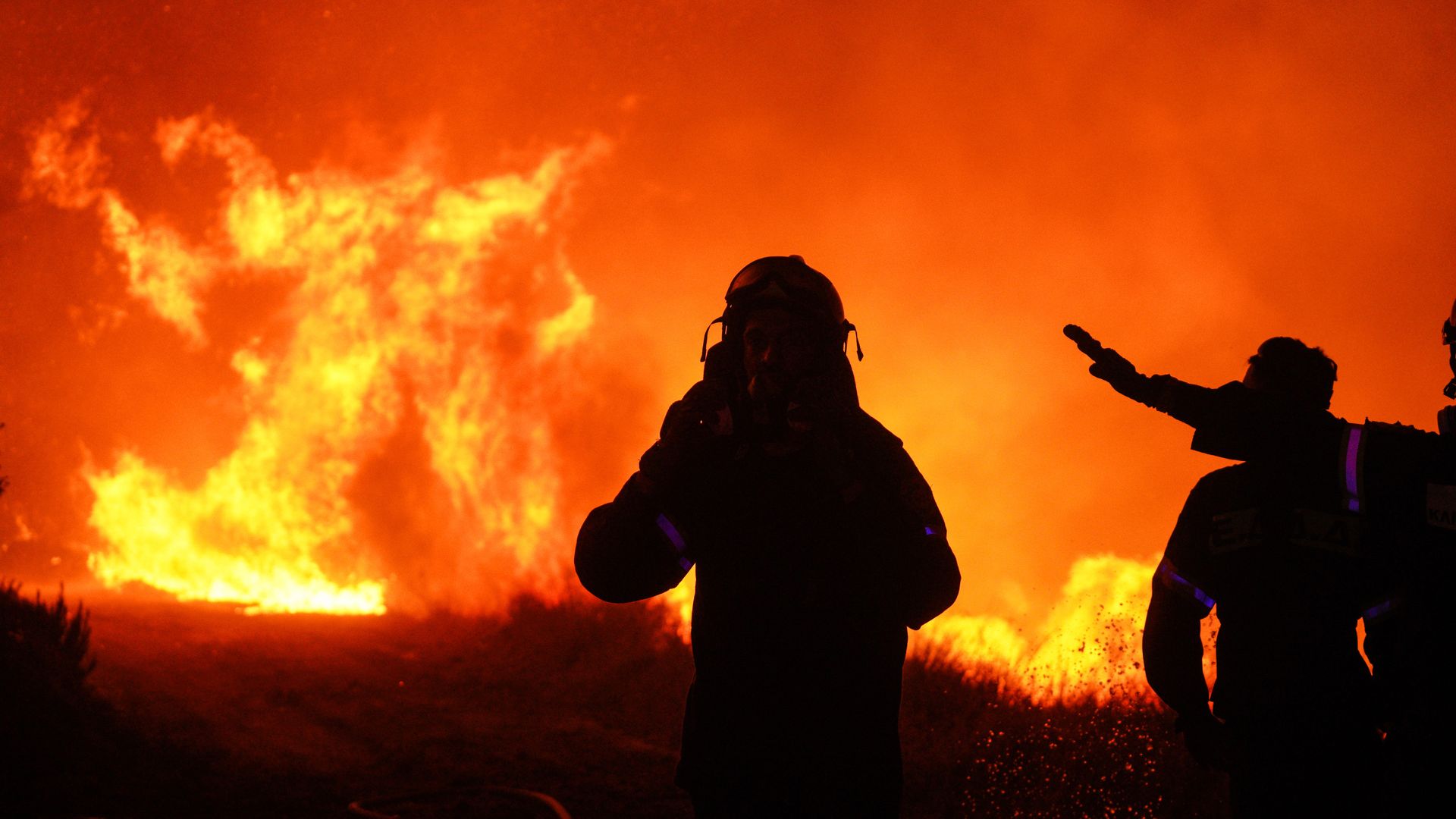 Bright orange flames from a wildfire burning near Athens appear in front of firefighters. 