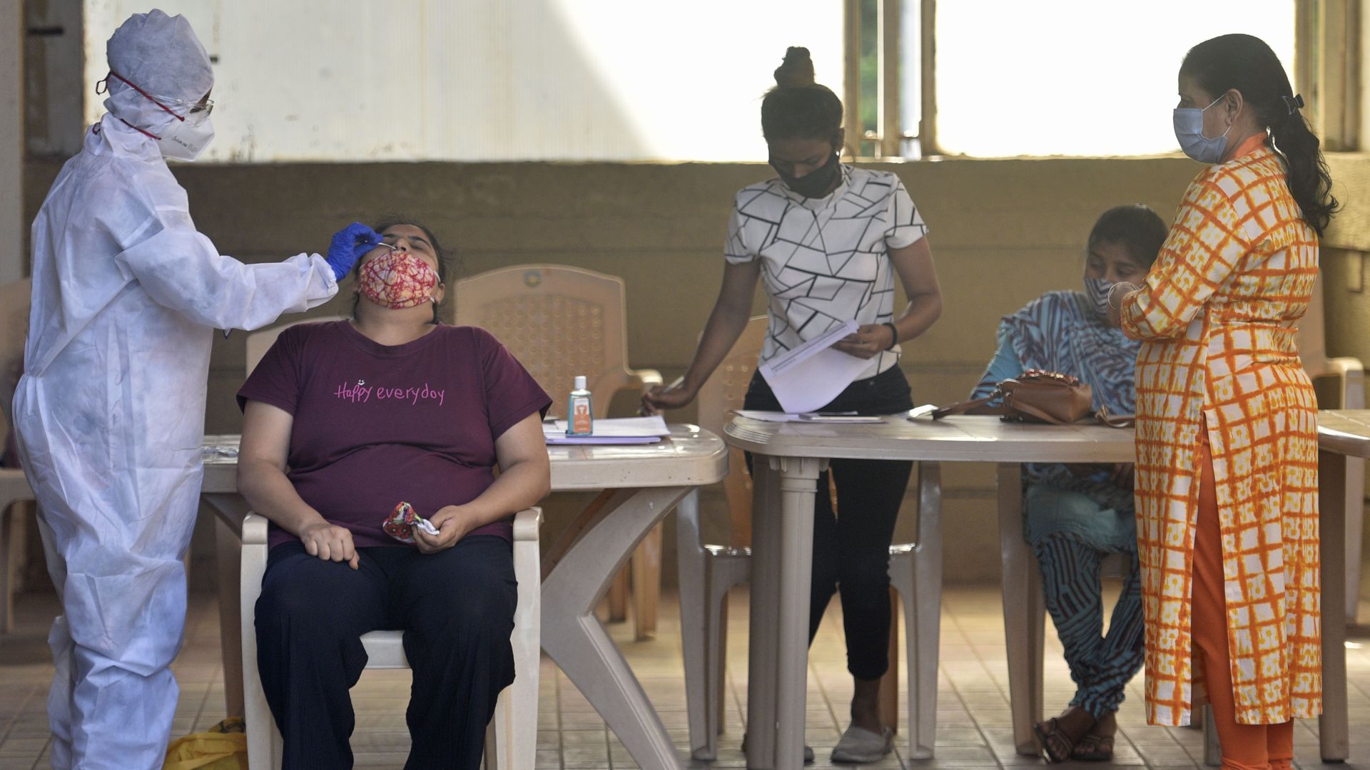 A healthcare worker in full PPE administers a COVID swab test