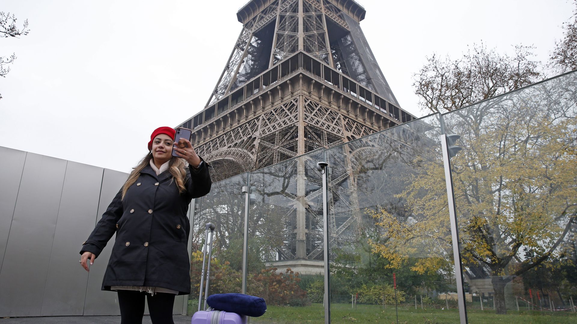Woman with suitcase takes selfie in front of Eiffel tower.