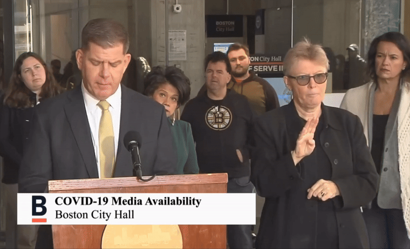 A gif showing a random Bruins fan and his friend stumbling onto a Boston COVID-19 press conference as Boston Mayor Walsh speaks at the podium on March 18, 2020. 
