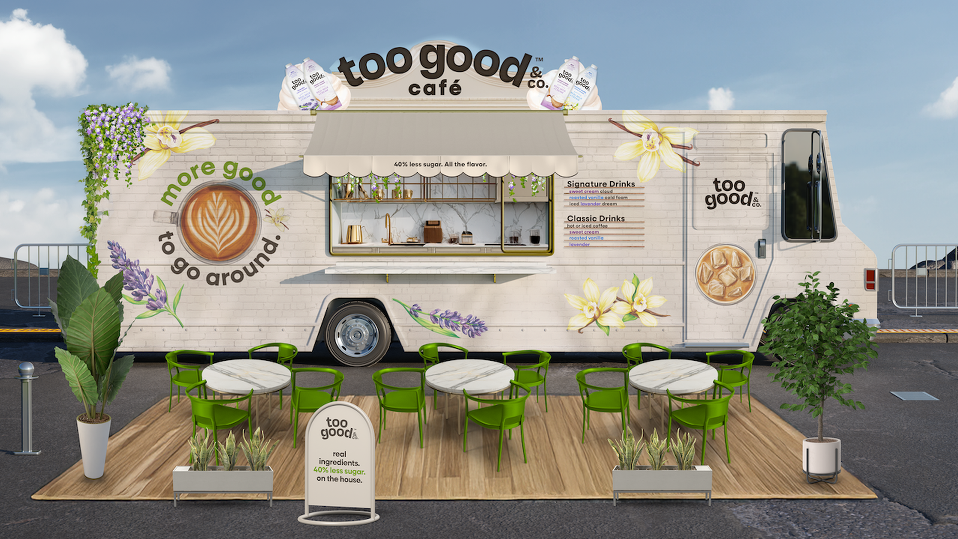 White brick food truck labeled 'too good café' with a beige awning and flower murals; outdoor wooden platform with white marble tables, lime-green chairs, and potted plants.