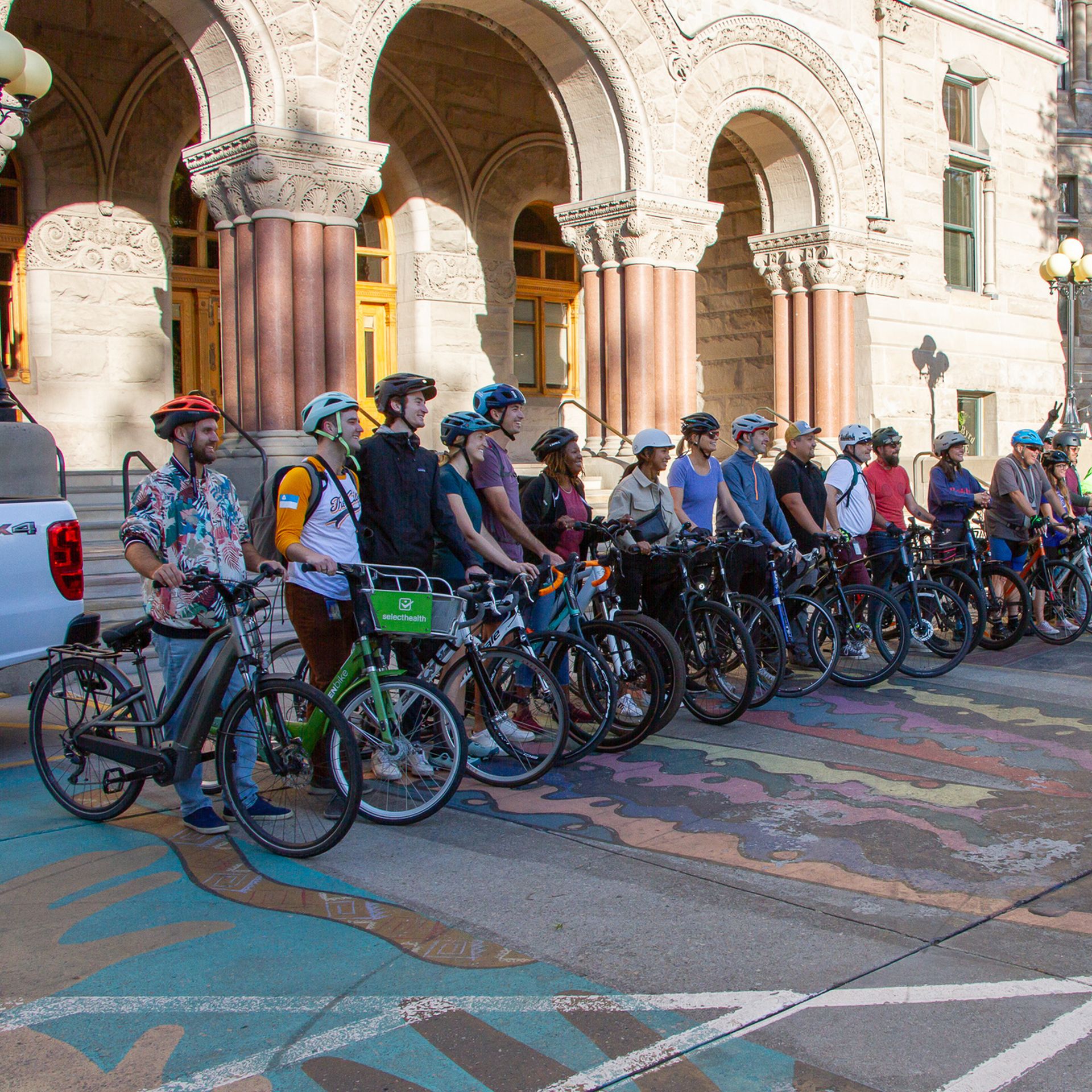 A couple dozen cyclists line up with their bikes in front of a building.