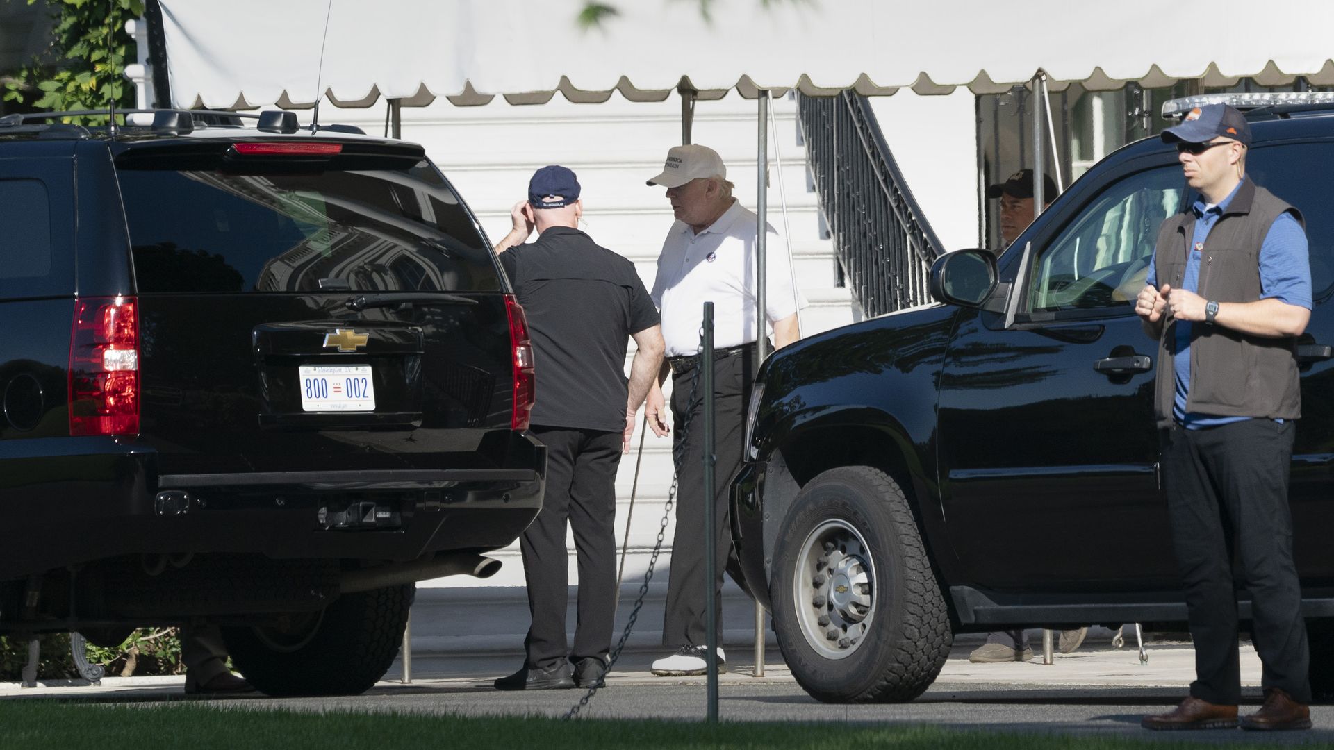 In this image, Trump wears a baseball cap and gets into a black SUV