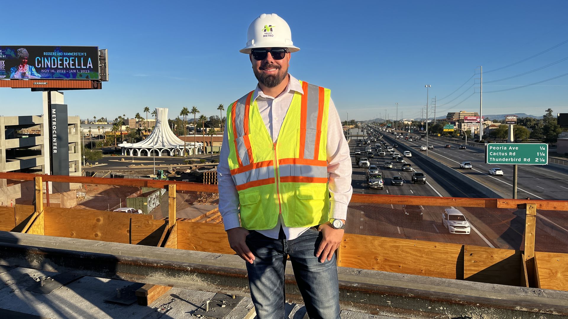 A man in construction gear stands on a bridge over a freeway.