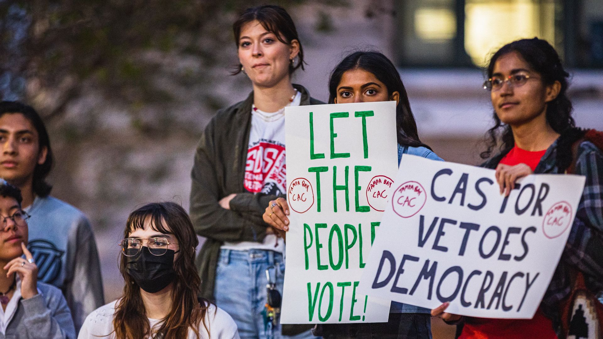 Protesters holding signs reading "let the people vote" and "Castor vetoes democracy"
