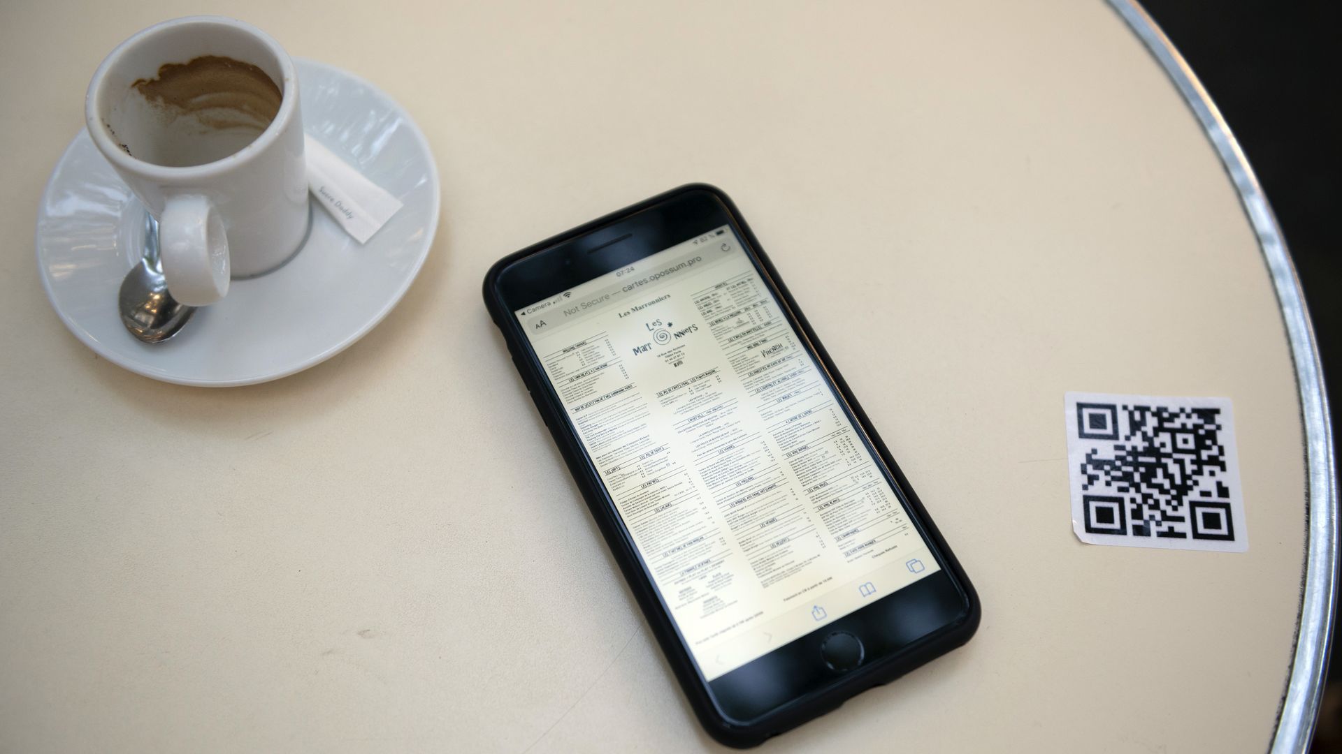 A cellphone, a printed QR code and a cup of coffee on a table 