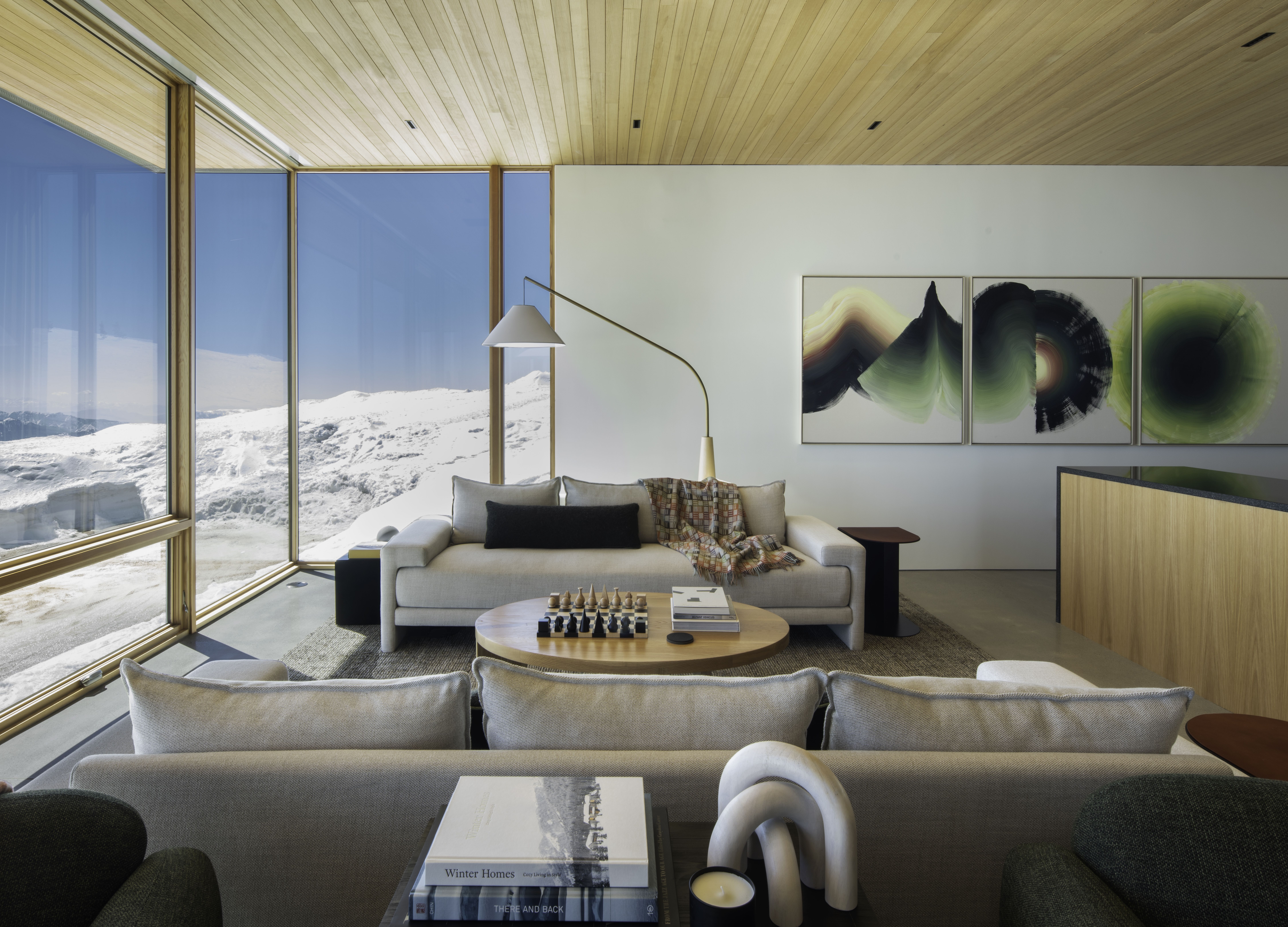 A modernist living room with walls of glass looking onto a snowy hilltop.