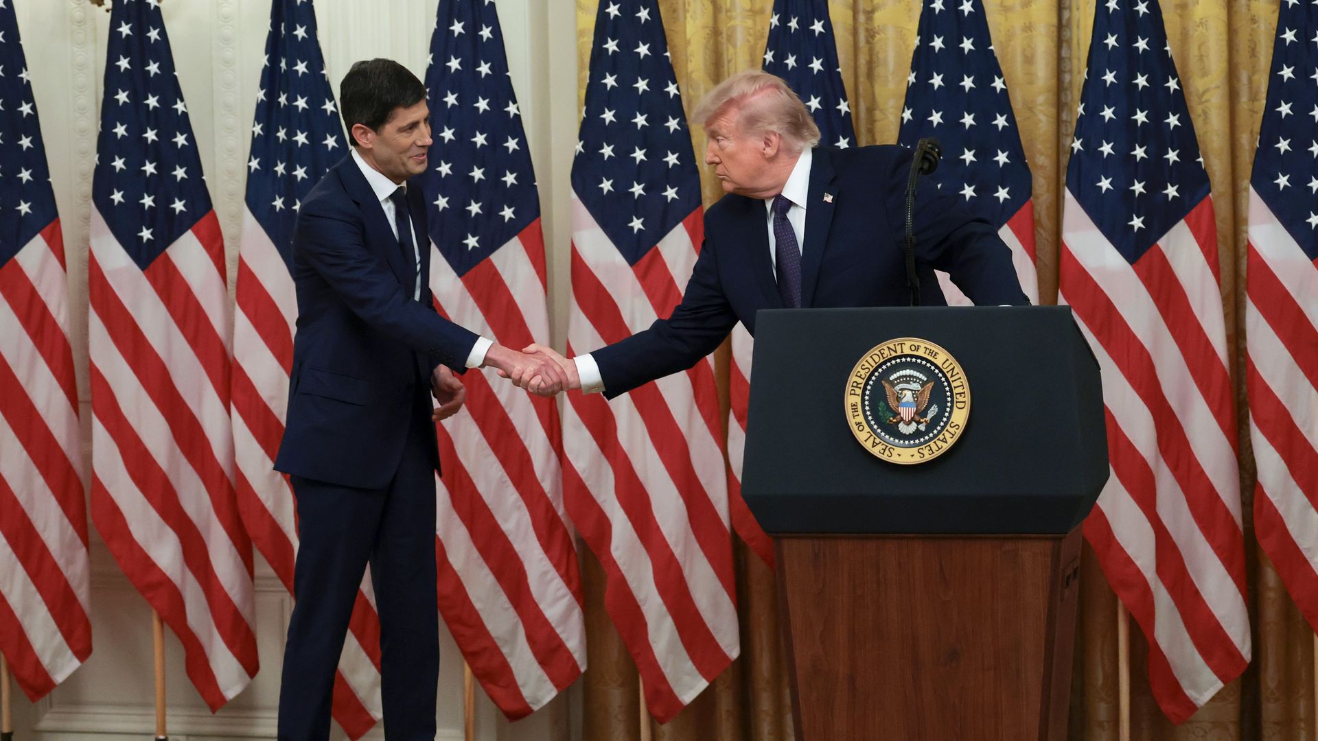 Kevin Warsh at left shaking hands with President Trump at a podium