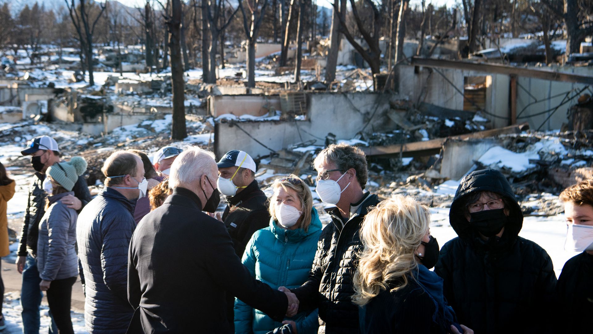 Photo of Joe and Jill Biden shaking hands and speaking with local residents as they stand in front of rubble