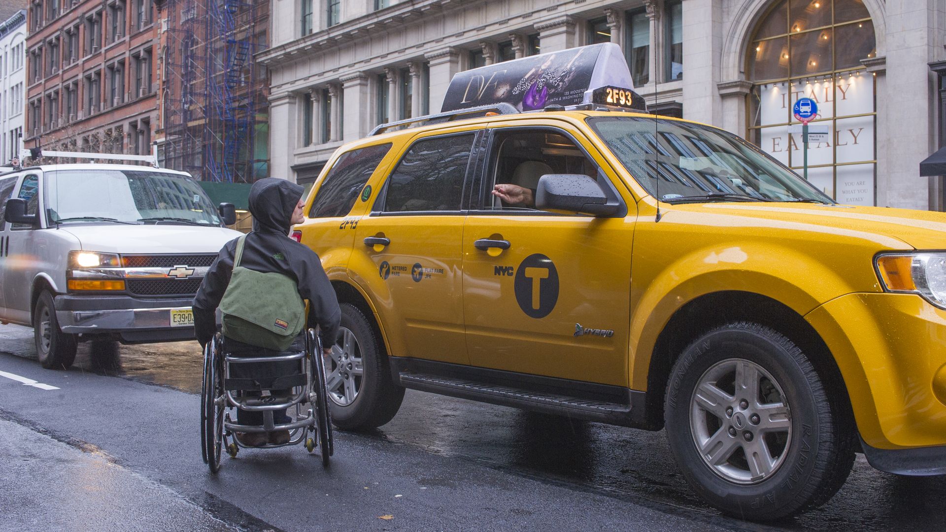 A man using a wheelchair hails a taxi.