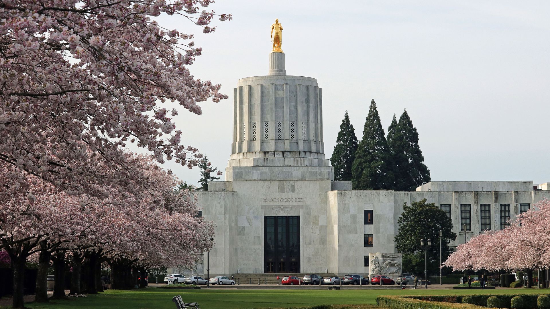 A photo of a white building with marble and golden statue of a person on the top.