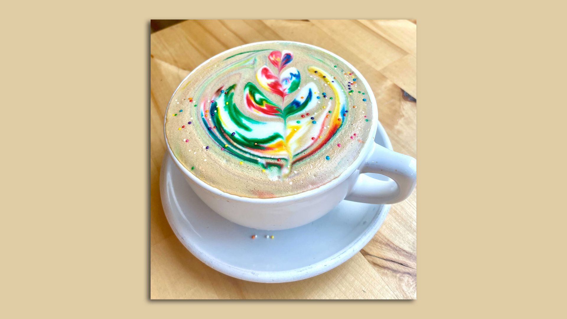 latte with rainbow design and candy sprinkles on top on wooden table