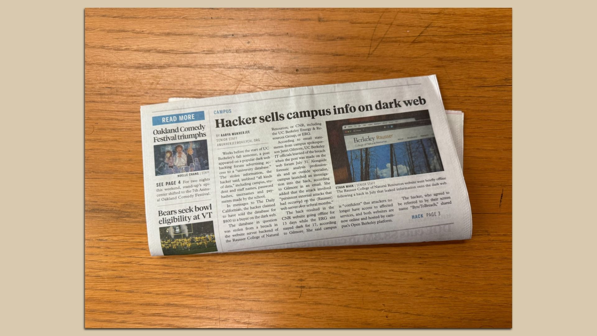 Folded newspaper on a wooden surface with headlines about a hacker selling campus info on the dark web, Oakland Comedy Festival, and college football eligibility at VT.