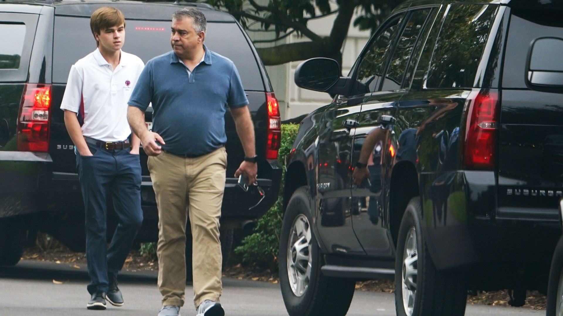 David Bossie wearing khaki pants walks towards a large black SUV