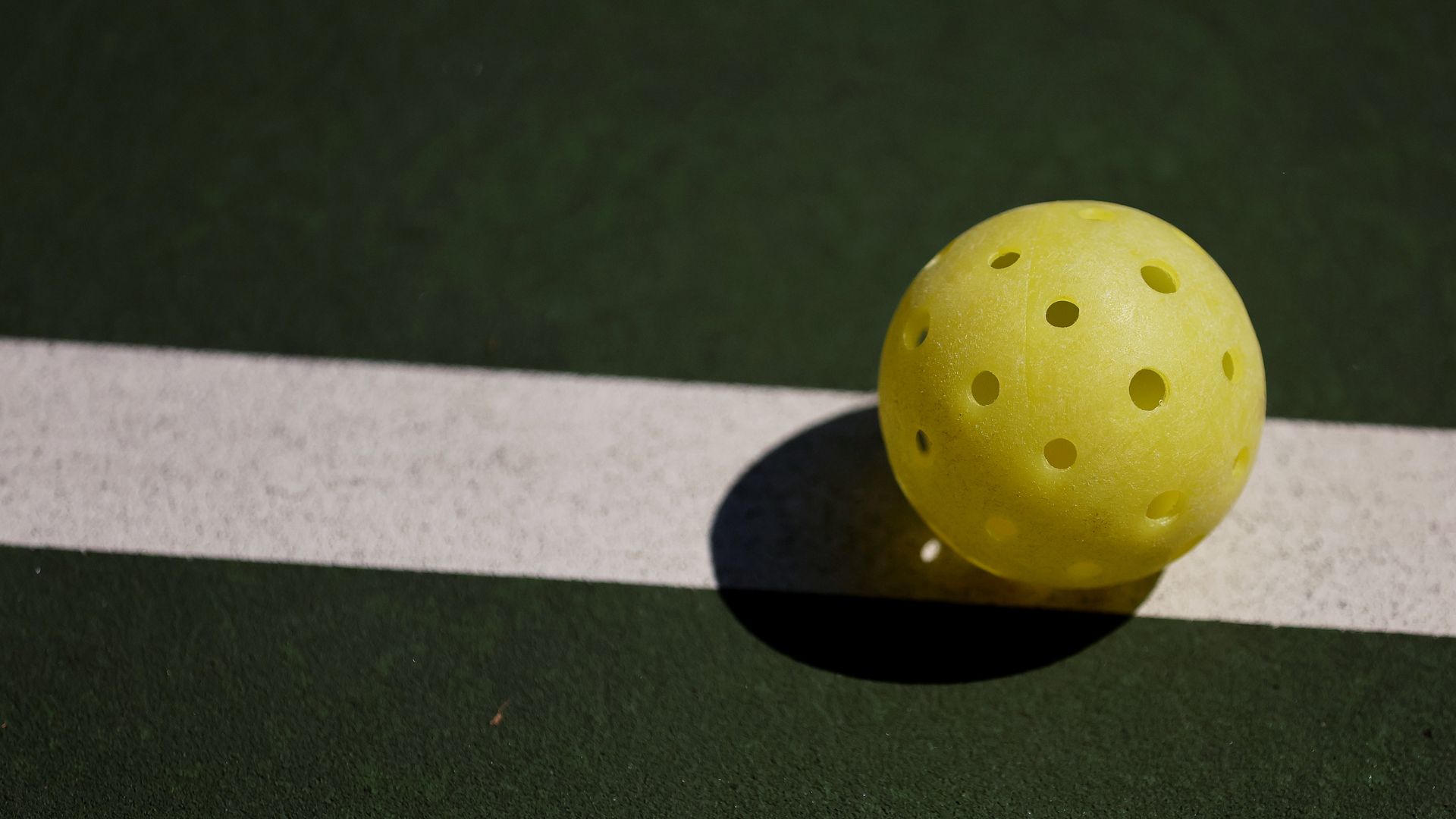 A pickle ball sits on a pickle ball court.