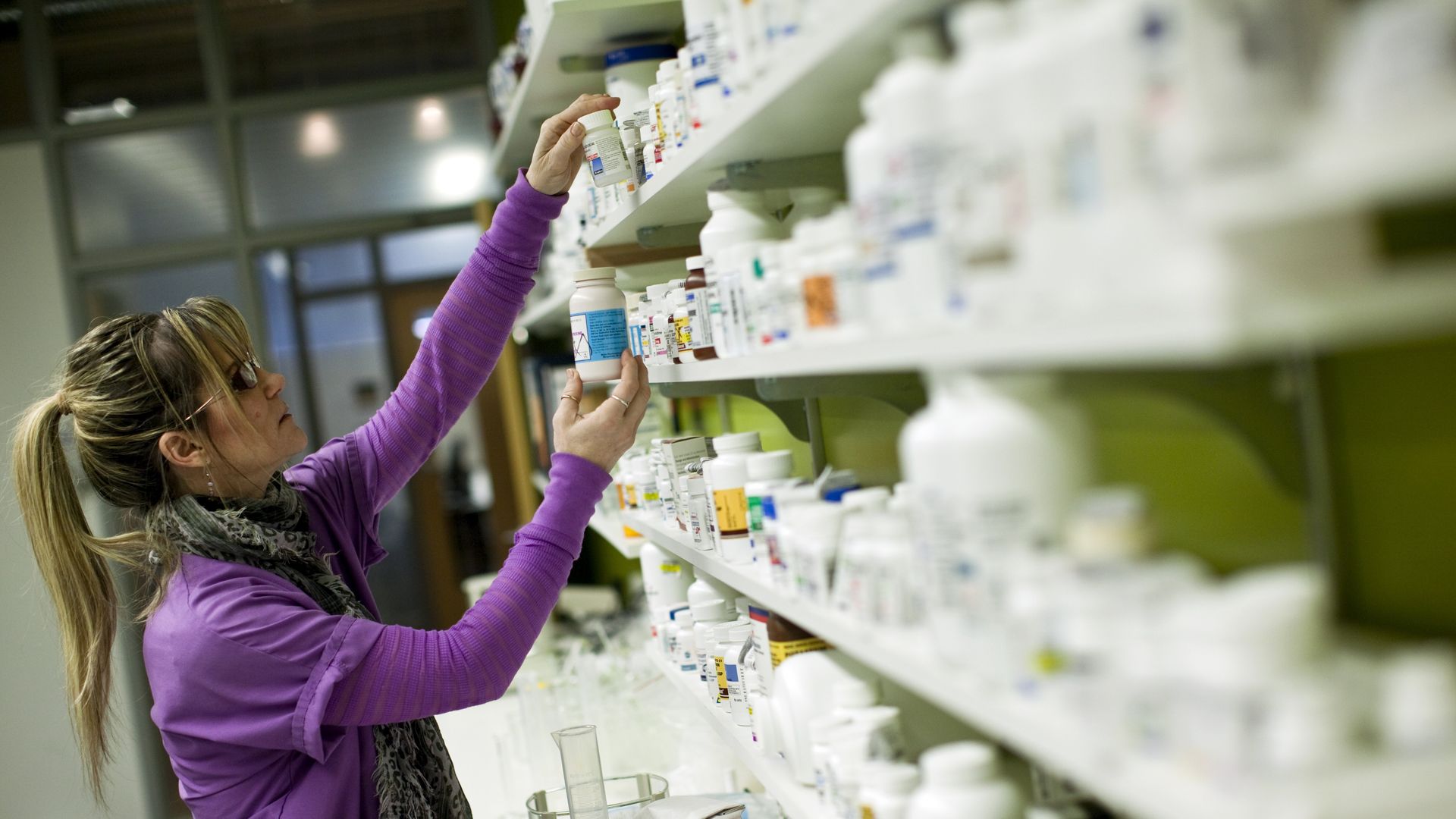 A pharmacy technician looks at prescription pill bottles on shelves.
