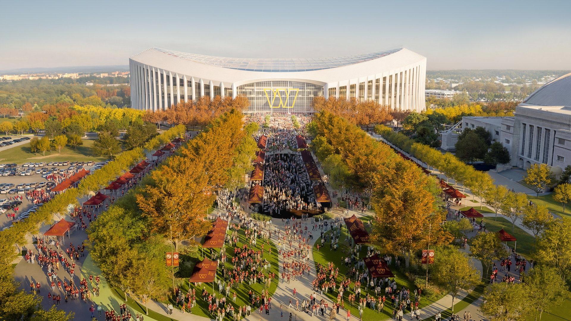 An architectural rendering showing an aerial view of a curved white Commanders stadium building with a glass entrance, surrounded by autumn trees. A large crowd walks along a central avenue with maroon tents for an outdoor campus event.