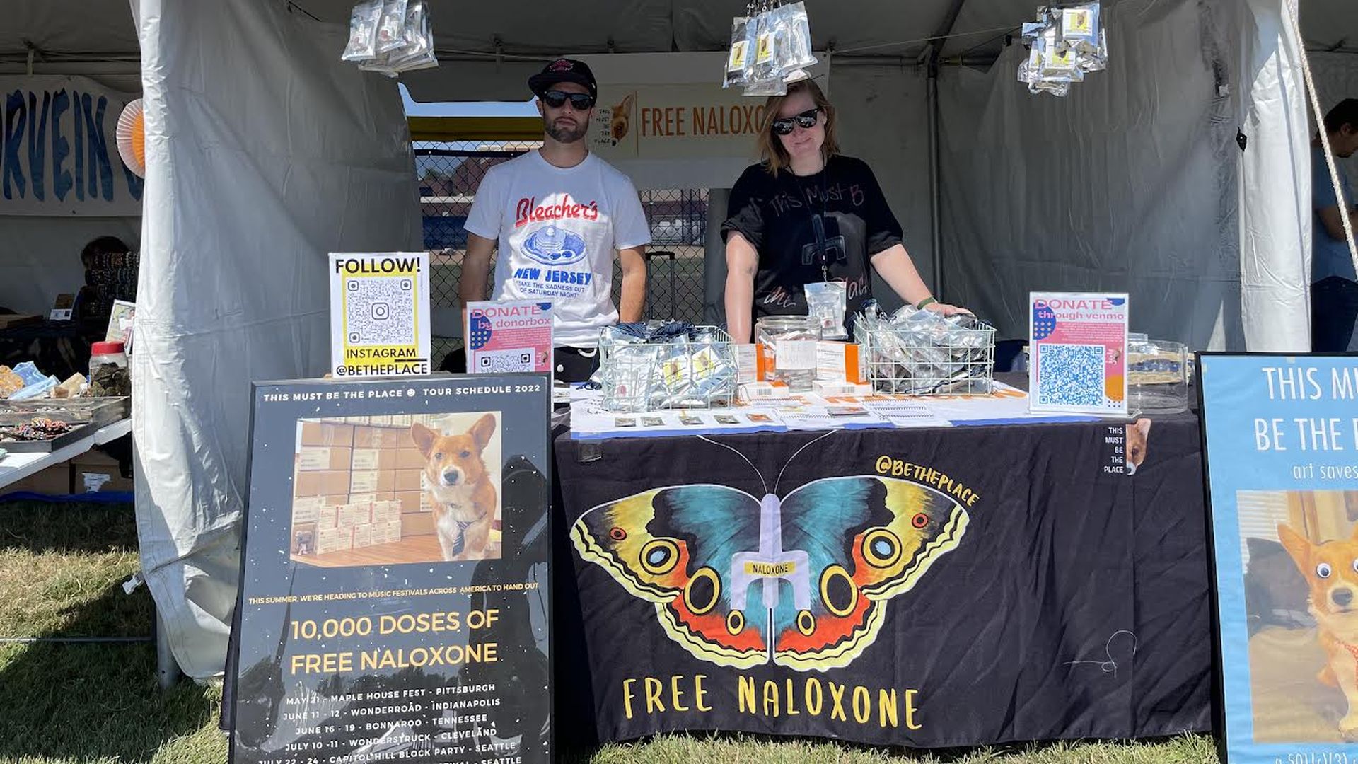 Two non-profit founders are seen at a music festival table distributing free naloxone.