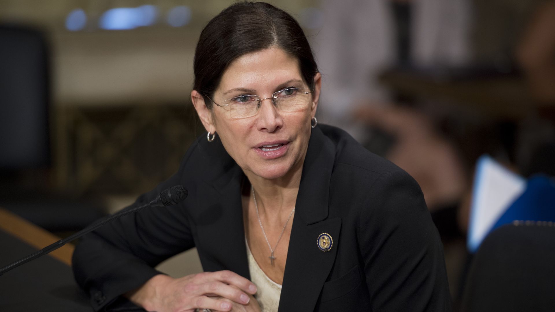 Mary Bono sitting in the house of representatives with suit and glasses on. 