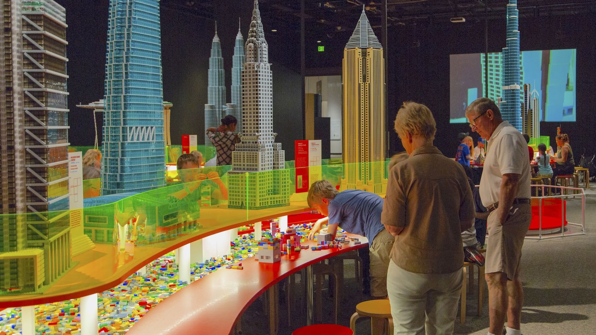 A big clear table topped with Lego skyscrapers and play / build area underneath 