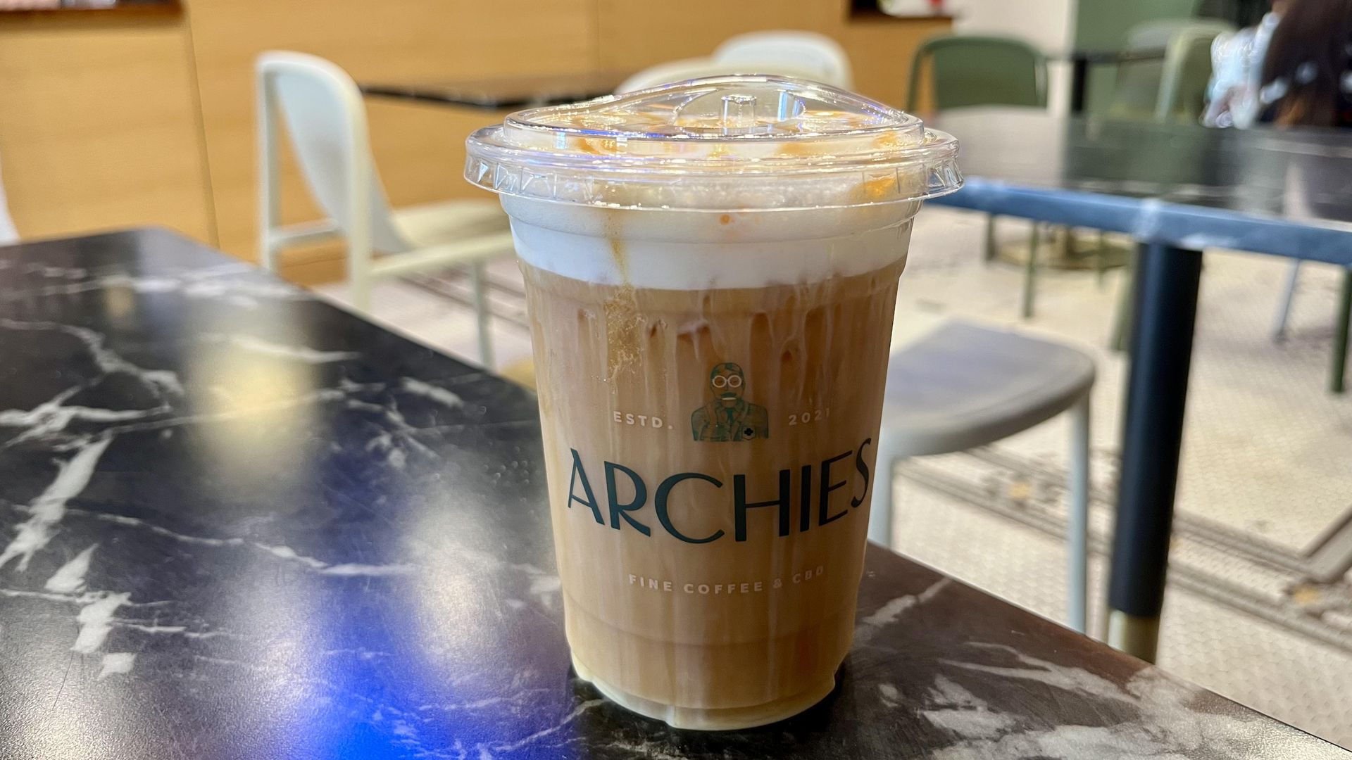 A light colored coffee with a cold foam on top dripping with caramel sauce.