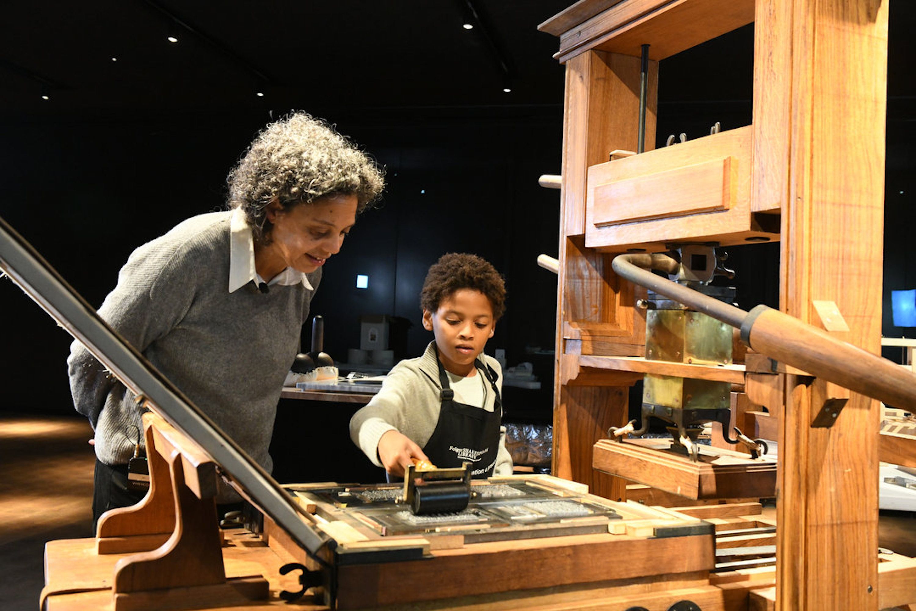 A woman and young boy play with a 17th century wooden printing press