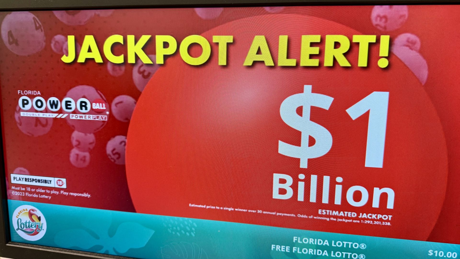 Screen showing a red background with yellow text "JACKPOT ALERT!" and white text "$1 Billion" for Florida Powerball lottery, with lottery balls faintly visible behind.