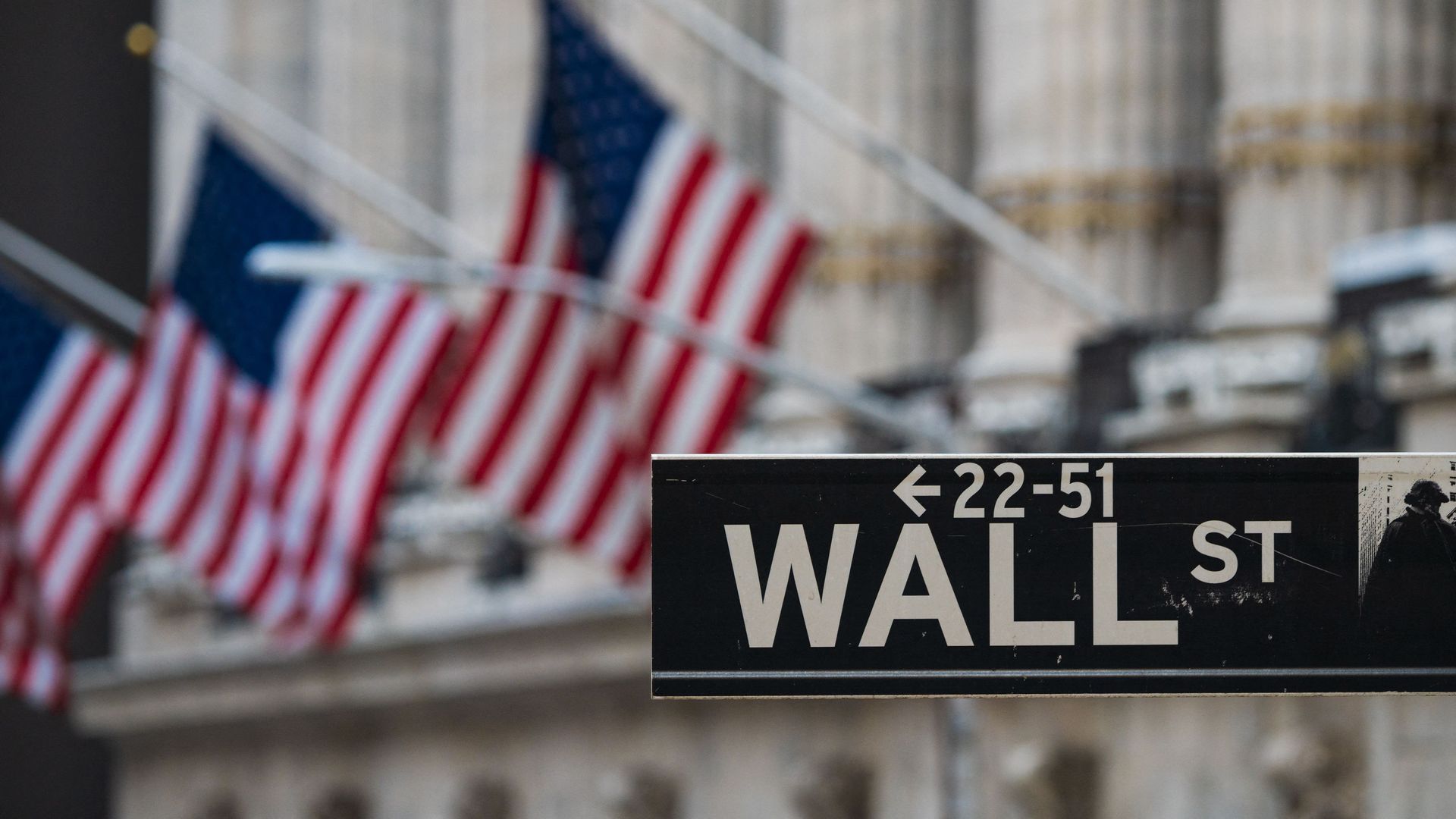 Photo of a Wall St sign next to a building that has an American flag hanging on one side