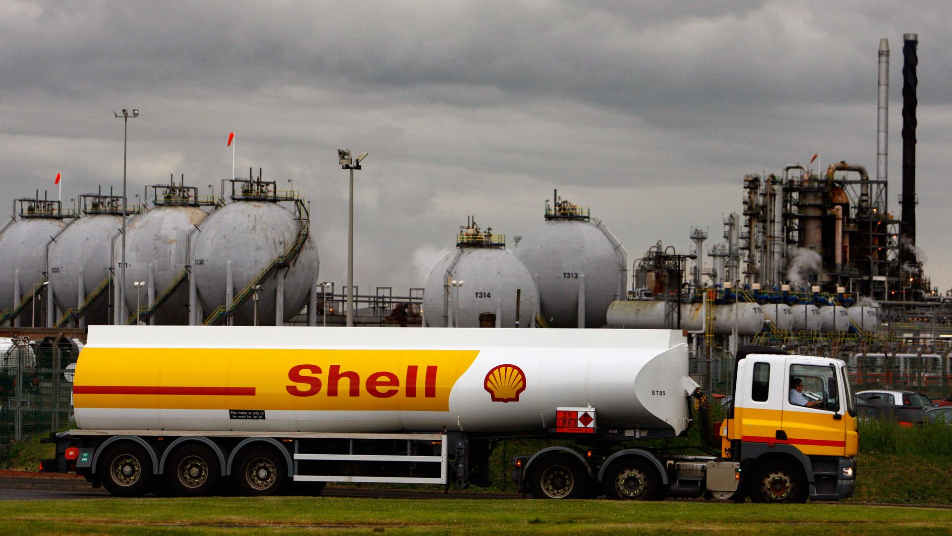 In this image, a Shell brand tanker sits in front of a plant on a cloudy day. 