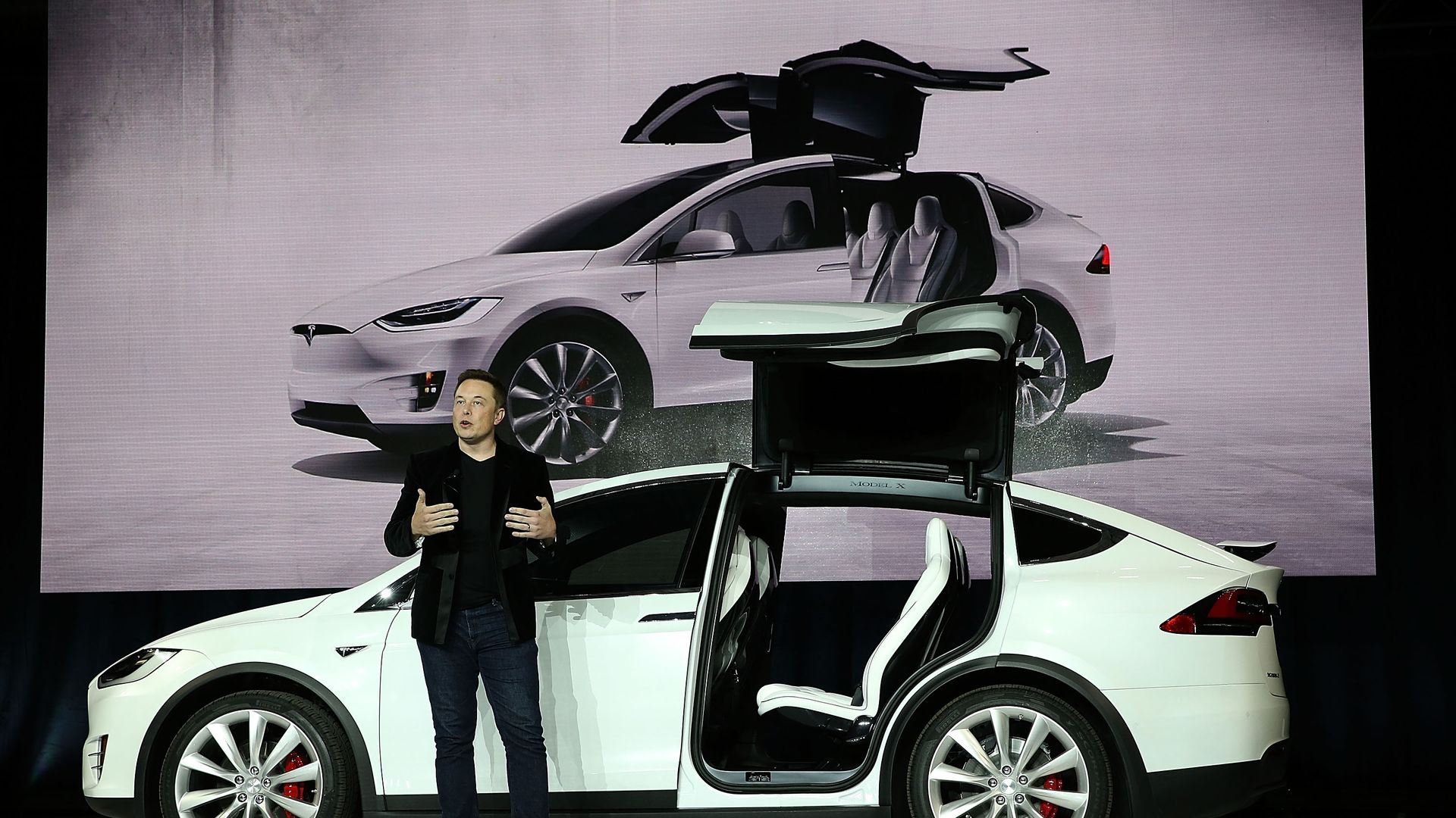 Elon Musk speaking in front of Tesla car