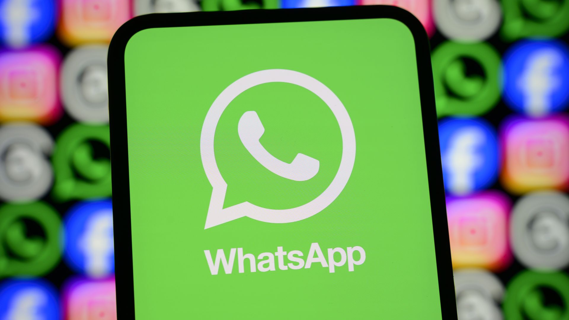 The WhatsApp logo appears on a smartphone screen in front of a screen showing icons for Facebook, Instagram, WhatsApp, and other Meta apps.